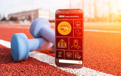 Smartphone mit geöffneter App, im Hintergrund liegen Hanteln